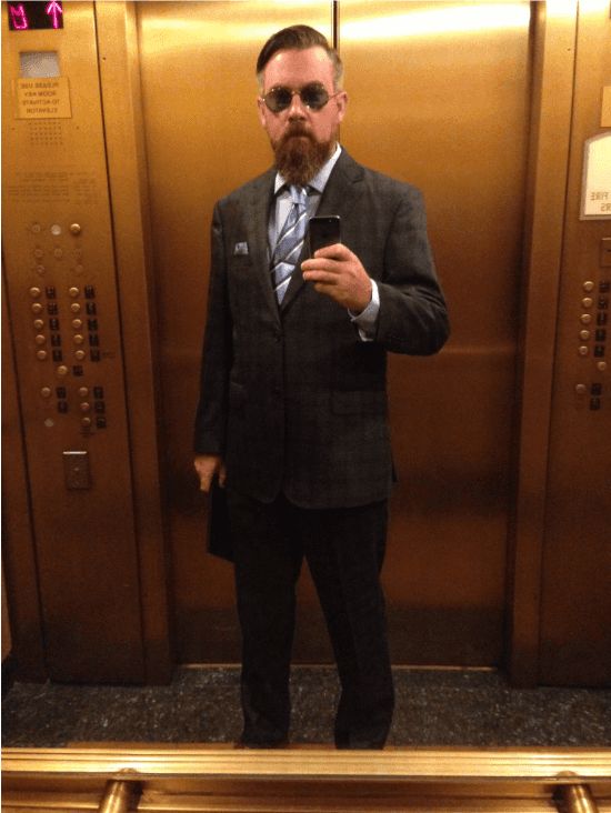 Taking a selfie, in an elevator in Manhattan, and wearing a suit.