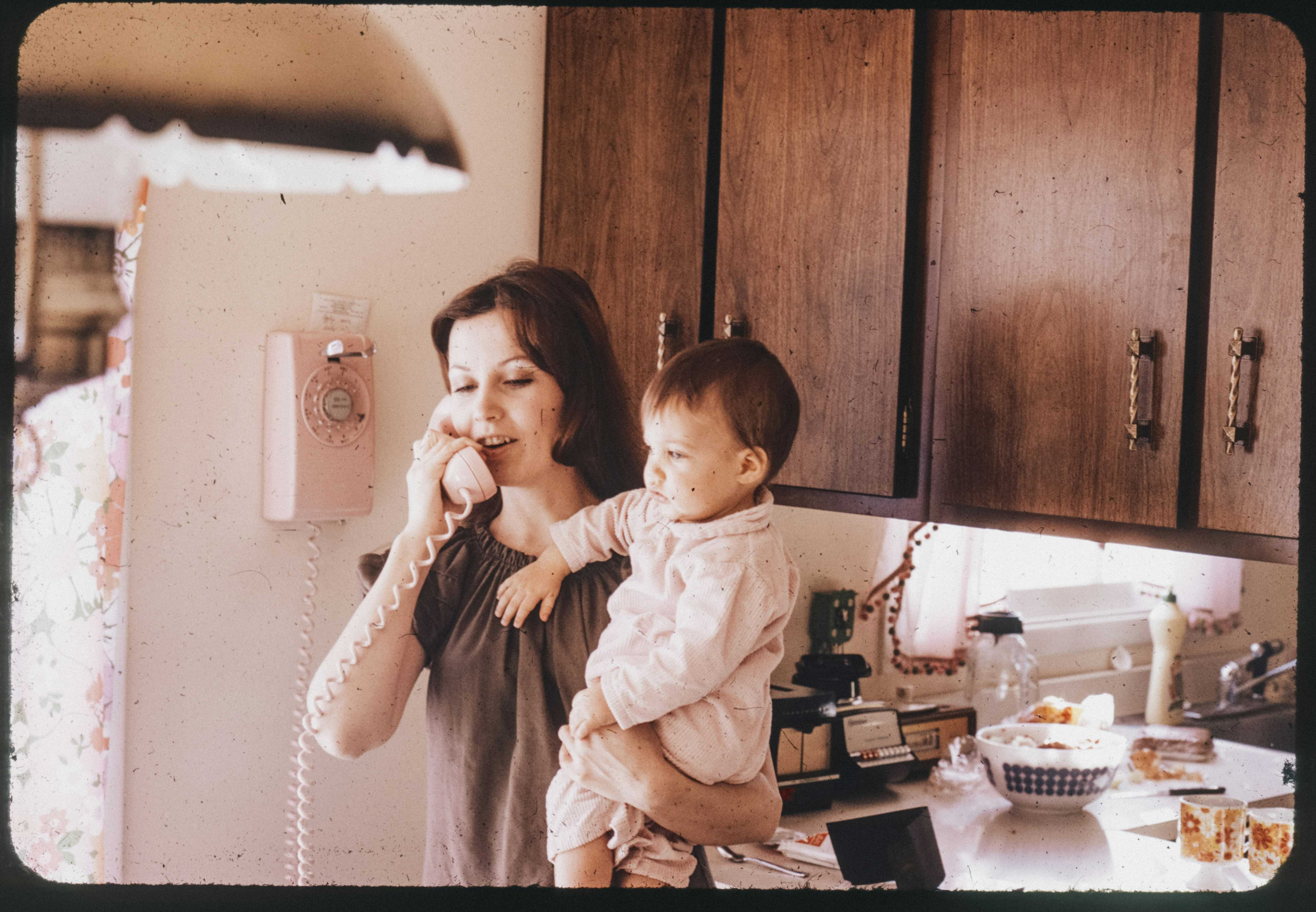 Mother holds her baby while talking on the phone.
